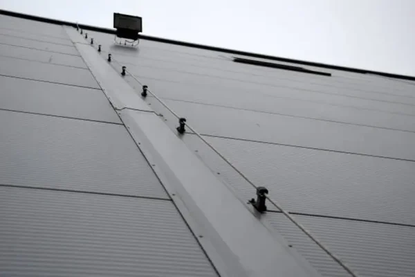 The lightning conductor is used to protect buildings from lightning, which can damage the house or industrial hall. grounding wire routing along a gray metal sheet facade. plastic holders